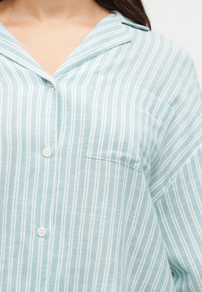 Femme portant une chemise à rayures verticales bleu clair et blanc avec une petite poche poitrine et un col décontracté.