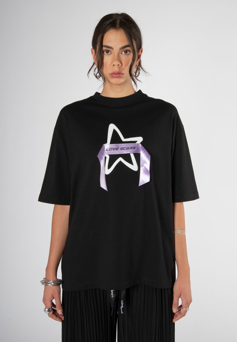 Camiseta negra de gran tamaño con un gráfico de estrella blanca y el texto "LOVE SCARS" en un diseño de cinta púrpura, con mangas cortas y cuello redondo.