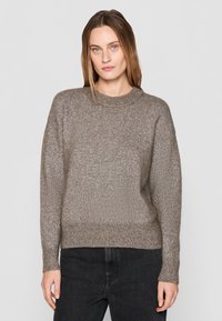 Pruun kudumipullover läikiva tekstuuriga, ümmarguse kaelusega ja vabalt istuv; omadused ribakujulised varrukad ja alläär, koos tumedate teksadega.