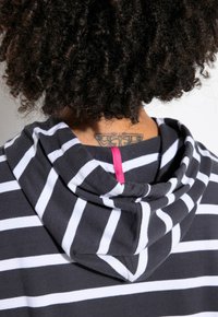 Felpa a righe con strisce bianche e nere, caratterizzata da un anello di colore rosa al collo e una morbida texture in cotone.