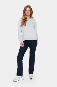 Felpa grigia chiara con logo rosa, abbinata a pantaloni blu scuro e sneakers bianche. Tessuto morbido, vestibilità casual e design semplice.
