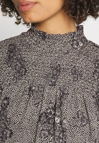 Schwarz-weißes, floral gemustertes Gewebe mit hohem Kragen und gefälteltem Design. Verfügt über eine gepunktete Textur und komplexe florale Akzente.