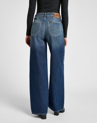 Wide-leg blue jeans made of denim with a faded lower leg, featuring a brown leather logo patch at the waistband and two back pockets.