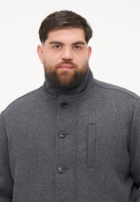 Caban gri din lână cu guler înalt, cu închidere prin nasturi și detaliu de buzunar ascuns pe piept. Textură netedă.