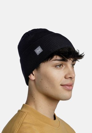 Gorro negro acanalado con un parche de logo, que presenta un ajuste ceñido y tejido texturizado. Lo lleva una persona con cabello corto y oscuro.