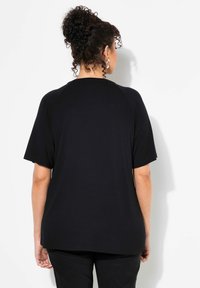 Camiseta negra de manga corta con un ajuste relajado, mangas raglán y una textura de algodón suave, con costuras mínimas y un escote redondeado.