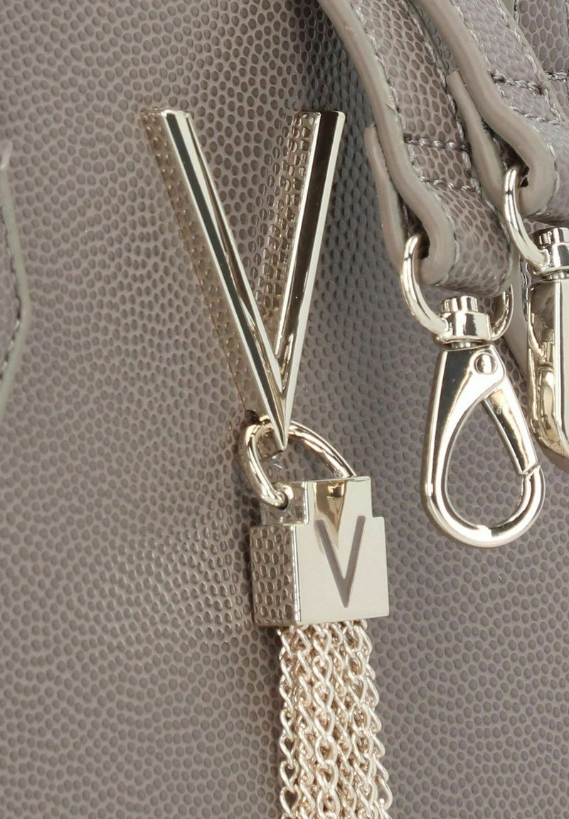 Detail van een grijze leren tas met textuur, voorzien van een gouden "V"-hanger en slot, met zilveren kettingaccenten en metalen hardware.