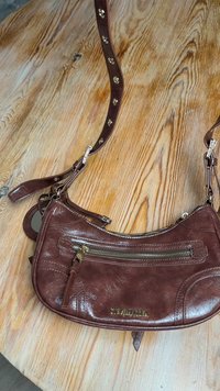 Braune Umhängetasche aus Leder mit strukturierter Oberfläche, ausgestattet mit einer Reißverschlusstasche, goldfarbenen Beschlägen und einem gemusterten Gurt.