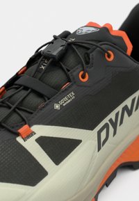 Μαύρο και γκρι αθλητικό παπούτσι με πορτοκαλί λεπτομέρειες, επωνυμία GORE-TEX, υφή υλικού και κομψό σχέδιο με σύστημα γρήγορης προσαρμογής κορδονιών.