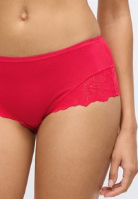 Κόκκινο βαμβακερό εσώρουχο hipster με λουλουδάτη δαντέλα στις πλευρές και λεία ζώνη μέσης, με λεπτομέρεια σε σχήμα κυματοειδούς άκρης.