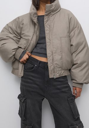 Personne portant une doudoune beige par-dessus un pull court foncé et un pantalon cargo noir taille haute avec de grandes poches latérales.