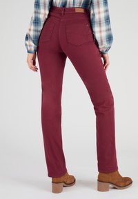 Jeans burdeos ajustados con cintura alta, que cuentan con dos bolsillos traseros. Combinados con botas de tobillo marrones y una camisa de cuadros.