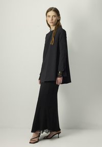 Black long-sleeve top with a relaxed fit, paired with a flowing black maxi skirt. The outfit features subtle gold accents on the sleeves.