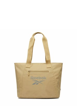Beżowa torba typu tote marki Reebok z dwoma paskami na ramię, przednią kieszenią na zamek oraz szarym logo Reebok umieszczonym na środku poniżej kieszeni.