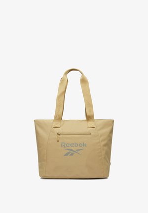 Bolso tote beige de Reebok con dos asas para el hombro, bolsillo frontal con cremallera y logotipo gris de Reebok centrado debajo del bolsillo.