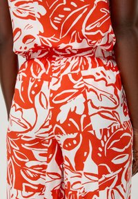 Czerwono-biała tkanina w wzory przedstawiające motywy liści. Projekt zawiera wyraziste linie i płynne kształty, a także elastyczny pas.