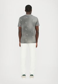 Grå t-shirt med små, lysegrå AX-logo mønstre, rund halsudskæring, parret med hvide bukser og lyse sko.