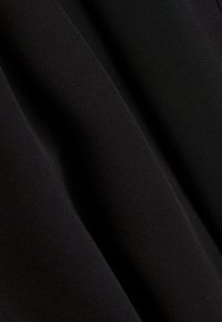 Czarna tkanina o gładkiej teksturze, ukazująca subtelne fałdy i różnice w świetle, co wskazuje na lekkim, elastycznym materiale.