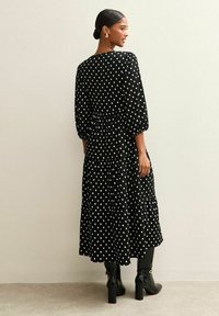 Zwarte maxi-jurk met een patroon van witte diamanten, lange mouwen, een getailleerde taille en gelaagde randen aan de zoom.