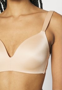 Nude, satin bra with a deep V-neckline. Smooth, seamless cups and adjustable straps. Minimalist design without hardware details.