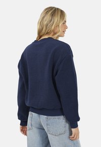 Marineblauwe fleece sweater met ribgebreide manchetten en zoom, met een relaxed fit en een gestructureerd oppervlak, van achteren gezien.