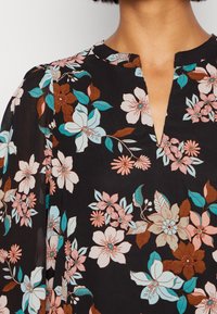 Sort blomsterbluse med lyserøde, blå og brune blomster, V-udskæring og blødt, letvægtsstof med gennemsigtige ærmer.