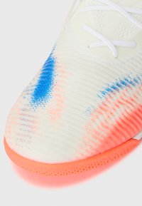 Leichtgewichtiger Sportschuh mit einem strukturierten weißen Obermaterial, das blaue und pinke Akzente aufweist, und einer lebhaften pinken Sohle. Die Schnürsenkel sind weiß.