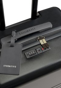 Zwarte harde koffer met uitschuifbare handgreep, voorzien van een combinatie slot, een soepele rits en een rechthoekig bagagelabel.