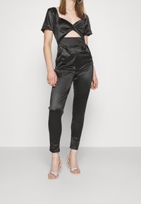 Mono de satén negro con mangas cortas, diseño recortado en la cintura y piernas ajustadas. Combinado con sandalias de tacón alto plateadas con tiras.