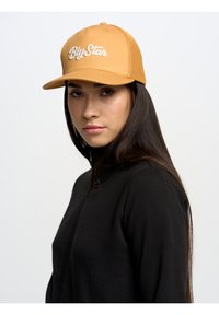 Gorra de béisbol naranja con bordado blanco "BigStar" y lados de malla, combinada con un suéter negro con cremallera. Textura de tela suave.
