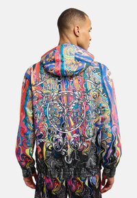 Kapuzenshirt mit lebhaften spiralförmigen Mustern in mehreren Farben, dekorativen Details und dem Namen "CARLO COLUCCI" auf der Rückseite.