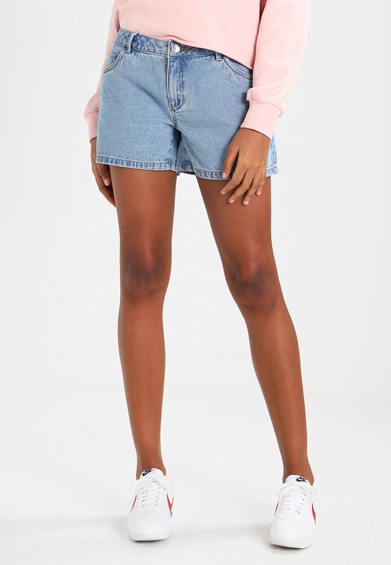 Denimshorts i ljusblått, med avslappnad passform, frampocketar och knappstängning, kombinerade med vita sneakers.