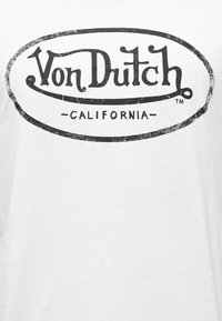 Λογότυπο Von Dutch σε φθαρμένη μαύρη γραμματοσειρά μέσα σε οβάλ περίγραμμα, με τη λέξη "California" γραμμένη από κάτω σε λευκό φόντο.