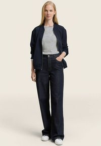 Navy bomber jacket, striped t-shirt, and dark wide-leg jeans with a high waist. Model stands in white sneakers on a neutral background.