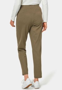 Olivgrüne, tapered Hose mit elastischem Bund, aus weichem Stoff. Kombiniert mit weißen Turnschuhen, Nahaufnahme des hinteren Designs.