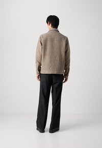 Chaqueta de camisa a cuadros marrón con cuello, cierre de botones y mangas largas; combinada con pantalones de pierna ancha negros y zapatos negros.