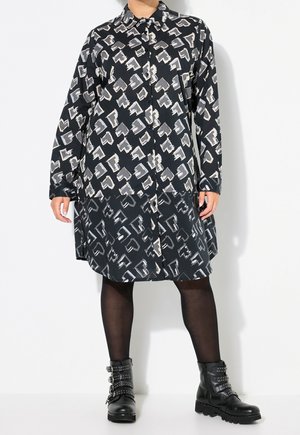 Robe boutonnée à manches longues avec motif noir et gris, associée à des collants noirs transparents et des bottines noires à boucles.