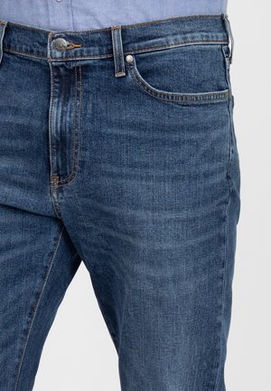 Jeansi din denim de culoare albastră închisă, cu o textură netedă, având cusături de cupru, închidere cu buton și buzunare frontale.