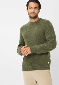 Grüner Strickpullover mit einem gerippten Rundhalsauschnitt, langen �Ärmeln und strukturierten Fleckendetails. Kombiniert mit hellen Cordhosen.