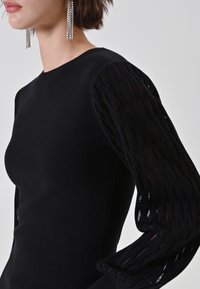 Schwarzer Pullover mit langen Ärmeln, enganliegendem Körper und strukturierten Ärmeln mit horizontalen Ausschnitten, der einen glatten Strickstoff und komplizierte Details zeigt.