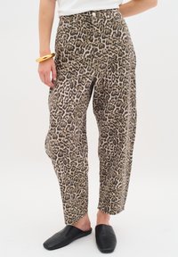 Kalhoty s leopardím potiskem v béžové a hnědé barvě, vysoký pas, volný střih a boční kapsy. V kombinaci s černými nazouvacími botami.