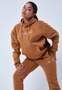 Bruine sweatshirt en bijpassende sweatpants van zachte stof, met een voorzak en witte logo-accenten op beide delen. Semi-figuuraccentuerende snit.