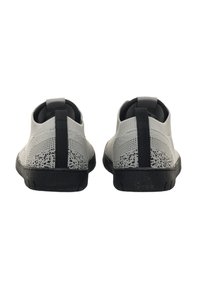 Ein Paar graue Strick-Schlüpfschuhe mit schwarzen Sohlen und vertikalen schwarzen Zuglaschen, von hinten auf einem weißen Hintergrund gesehen.