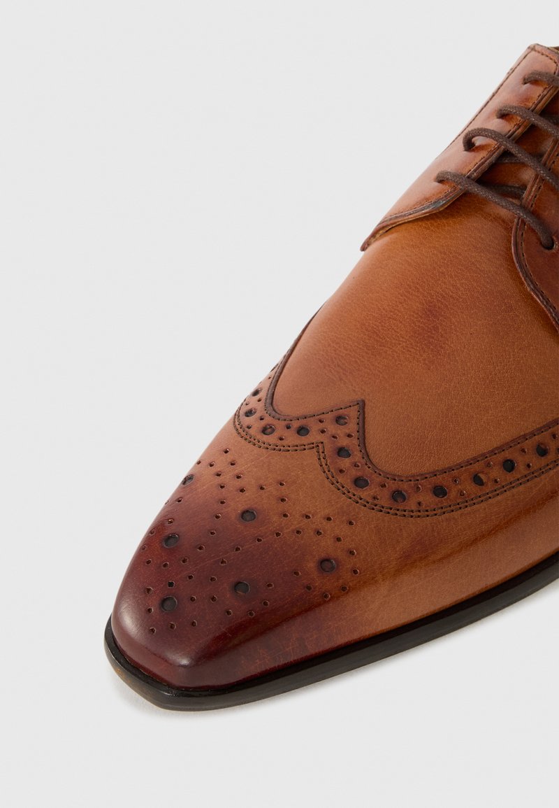 Brązowe skórzane buty eleganckie z ostrym noskiem, perforowanym wykończeniem i dekoracyjnym broguowaniem. Charakteryzują się polerowanym wykończeniem i sznurowanym zapięciem.