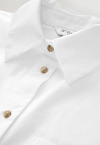 White button-up shirt made of cotton with a crisp collar and two light brown buttons. Smooth texture with no visible patterns or accents.