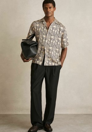 Cămașă cu mânecă scurtă în crem cu un model negru spiralat, purtată cu pantaloni negri și o geantă neagră, asortată cu pantofi maro.