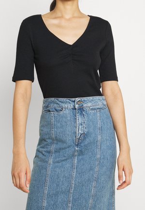 Czarny prążkowany top z krótkim rękawem i dekoltem w serek, z marszczeniem, połączony z jasnoniebieską, wysokowoską spódnicą jeansową z pionowymi szwami.