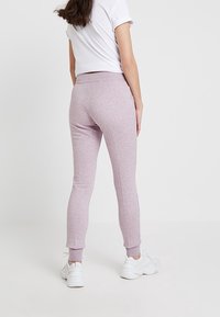 Lila träningsbyxor med en åtsittande design, mjuk textur, elastisk midja och ribbade ärmslut. Bärs med en vit t-shirt med kort ärm.