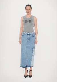 Siv basičen top z rebrastim vzorcem in napisom "Moschino Jeans", v kombinaciji z dolgo denim krilom z žepom in neobdelanim robom. Črne petke dopolnjujejo videz.