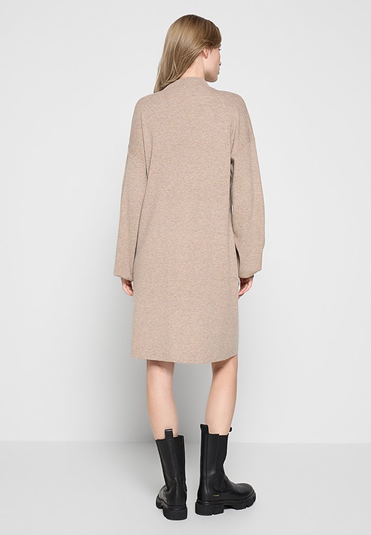 Langes, beige gestricktes Kleid mit rundem Ausschnitt und oversized Ärmeln. Kombiniert mit schwarzen Ankle Boots mit einer dicken Sohle.